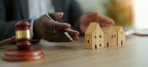 judge holding a pen in front of 3 wooden houses